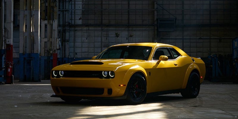 A low-angle shot of a bright yellow Challenger muscle car with black wheels, parked in a dark industrial garage.