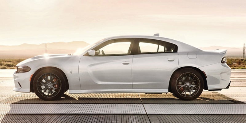 A white Dodge Charger sedan with black wheels and red brake calipers, viewed from the side on a sunny road.