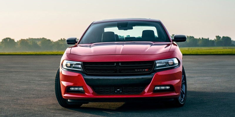 Front view of a red Dodge Charger parked on an asphalt road with green fields and trees in the background.