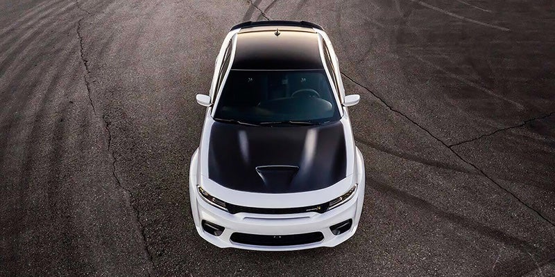 Front view of a white Dodge Charger with a black hood, glowing headlights, and sunset reflecting off the windshield.
