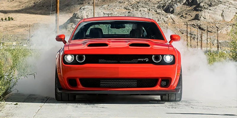 Full-frontal view of a bright red sports car with its headlights on, surrounded by white smoke.