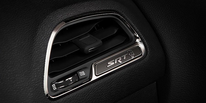 Vehicle air vent with chrome trim, 'SRT' logo, a snarling cat head icon, and vent controls.