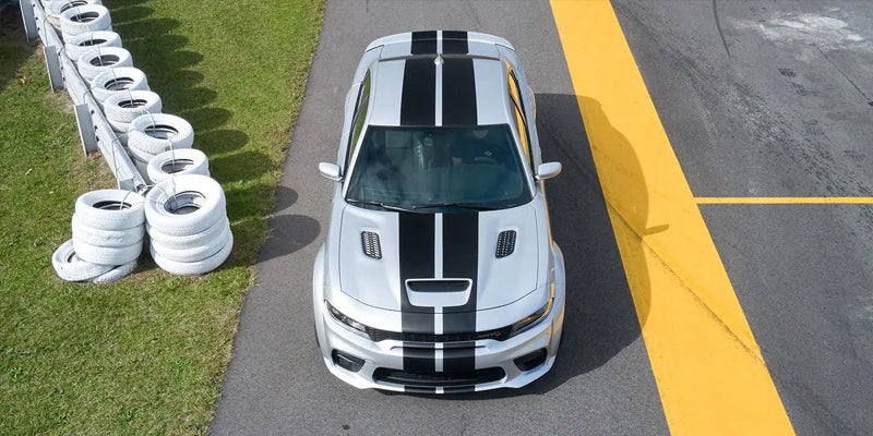 Overhead shot of a silver Dodge Charger with black racing stripes on a racetrack curve beside stacked white tires.
