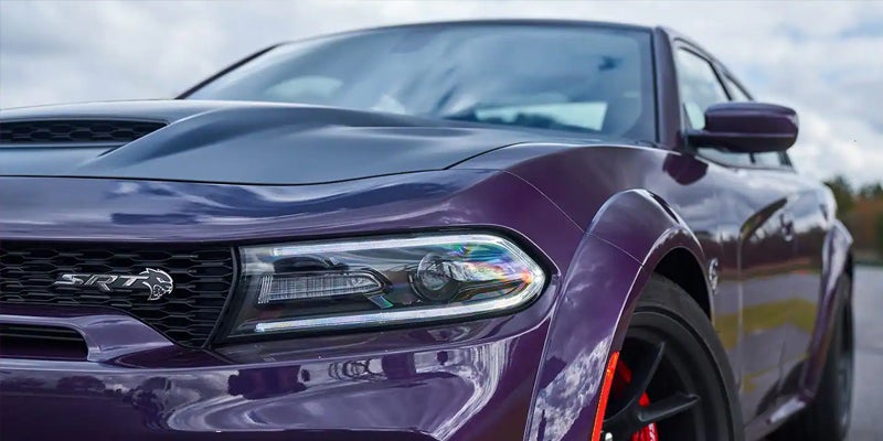 Close-up of a vibrant purple Dodge SRT Hellcat car, angled left, showing its front grille, headlight, and hood.