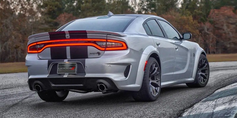Rear view of a silver Dodge Charger with black racing stripes and bright red taillights, on a race track curve.