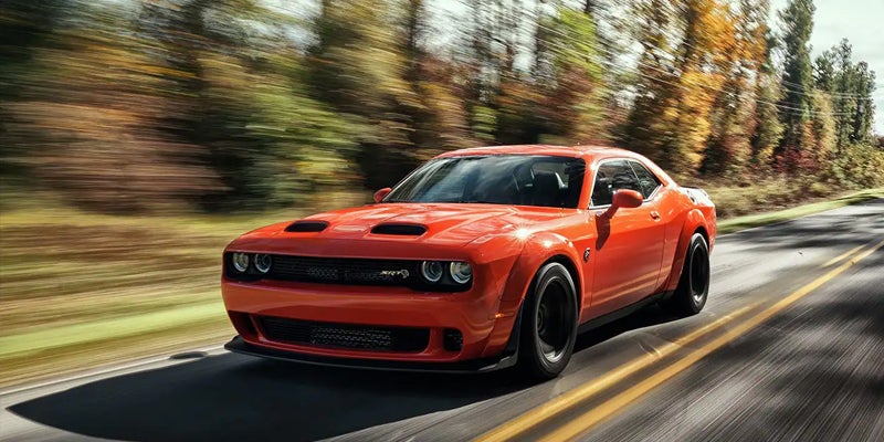 A powerful orange Dodge Challenger Hellcat SRT Redeye drives quickly down a country road with blurred trees.