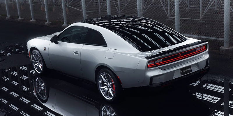 Rear view of a light gray 2024 Dodge Charger Daytona EV coupe with black roof, parked on a wet surface.
