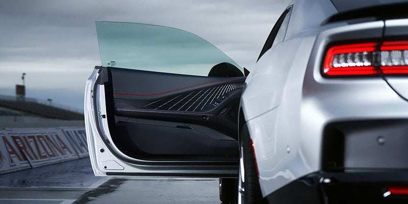 Rear view of a silver sports car with the passenger door open, parked on a racetrack in Arizona.