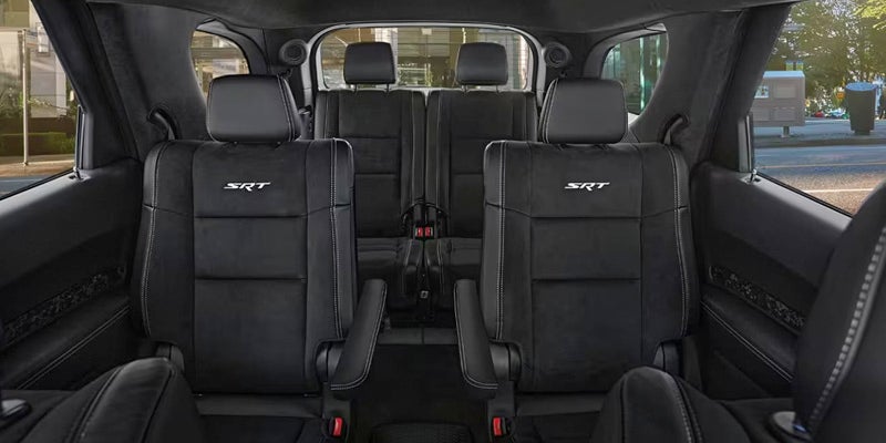 The interior of a black vehicle, featuring two rows of bucket seats with "SRT" embroidered on the headrests.