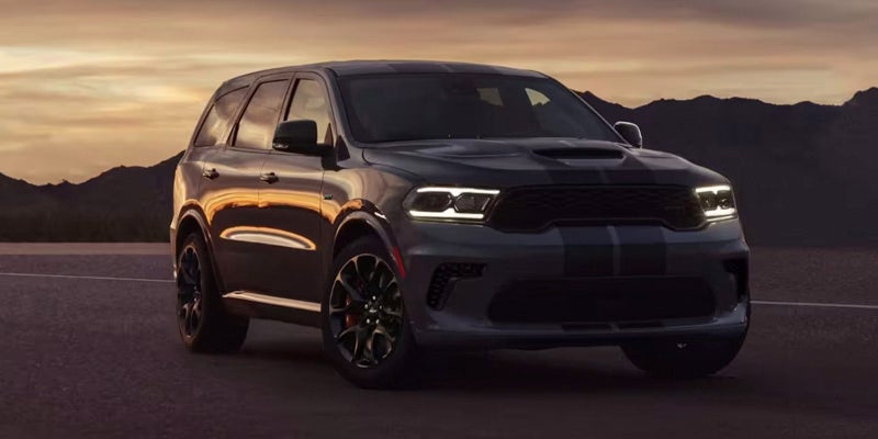 Dark gray SUV with black racing stripes on its hood and roof, parked on a road with mountains in the background.