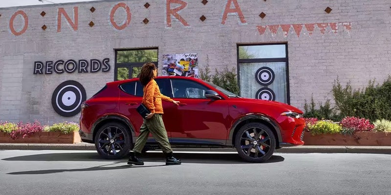 Woman in an orange jacket getting into a red Dodge Hornet parked in front of a building labeled "Records."