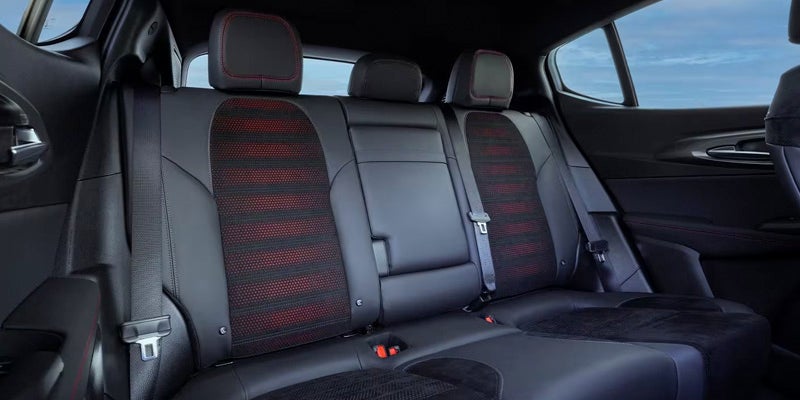 Rear car seats in black leather with red stitched trim and red-striped fabric inserts on the seatbacks.