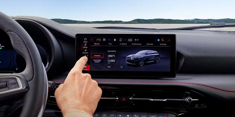 A driver’s hand interacts with a car’s infotainment system displaying vehicle information and a dark grey SUV.