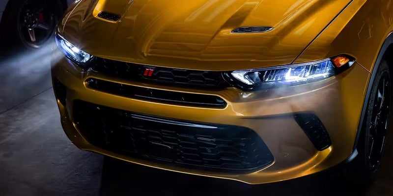 Front view of a shiny gold Dodge automobile showing headlights, honeycomb grille, and a red emblem.