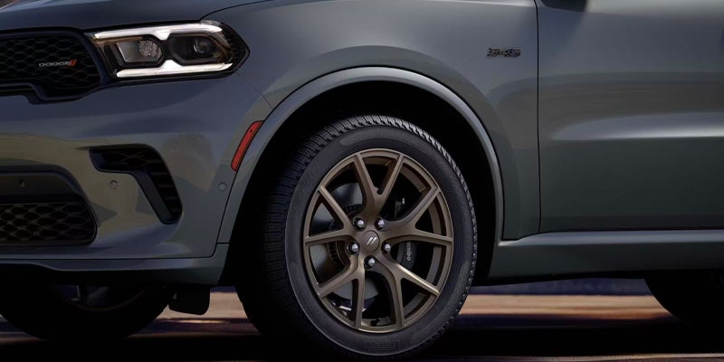 Front right side of a dark gray Dodge Durango SUV with its headlight on, showing the grille, a bronze wheel, and tire.