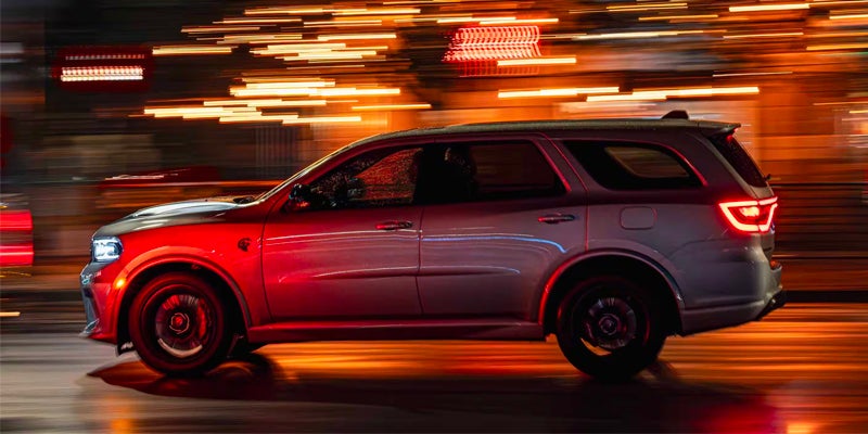 Gray SUV speeding at night with blurred streaks of orange and red light from streetlights.