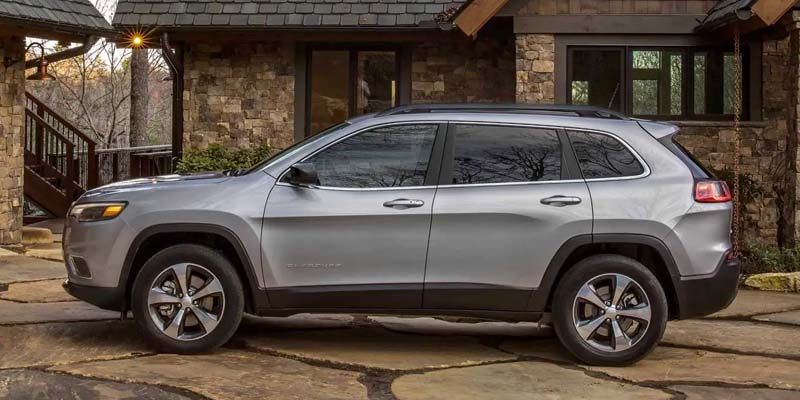 Silver 2021 Jeep Cherokee SUV parked on a stone driveway in front of a stone house.