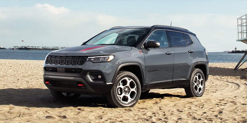 Dark gray Jeep Compass with red accents parked on a sandy beach, Pacific Ocean and offshore island in the background.