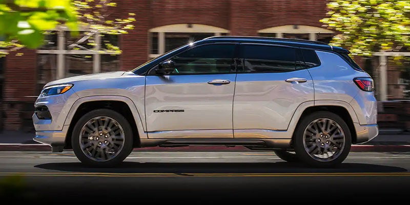 Silver Jeep Compass SUV driving past blurred buildings and trees.