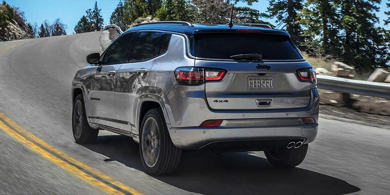Silver Jeep Compass driving away on a winding road with trees and mountains in the background.