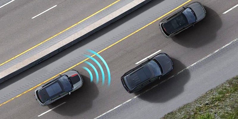Four cars on a multi-lane highway, with blue concentric waves indicating a blind spot warning system at work.