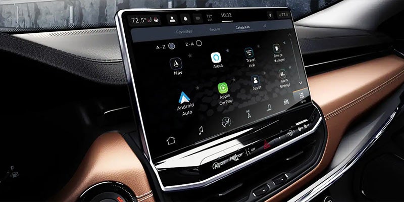 A close-up of a modern vehicle's dashboard with a black infotainment screen displaying various app icons.