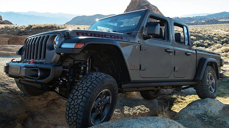 A dark gray Jeep Gladiator Rubicon pickup truck, with lifted suspension and aggressive tires, off-roading on rocky terrain.