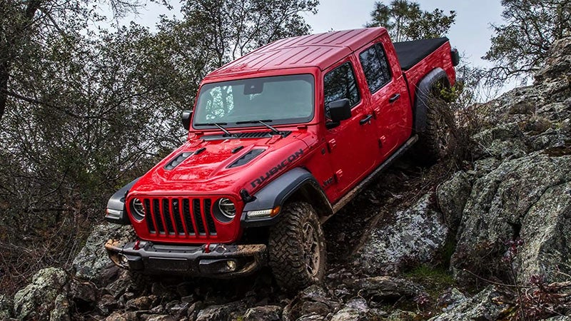 A red Jeep Gladiator Rubicon pickup truck off-roading on a rocky incline.
