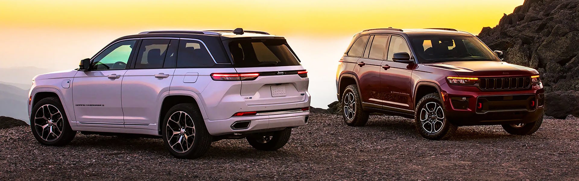 Two Grand Cherokees, a white one on the left and a red one on the right, parked on a rocky mountain.