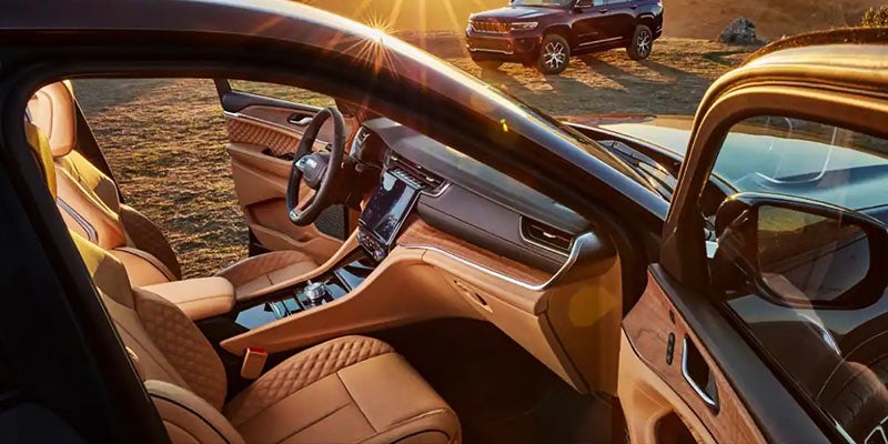 Luxurious tan leather interior of a Jeep Grand Cherokee with sun shining, another Jeep parked in the background.