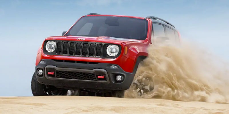 Red Jeep Renegade driving through sand, kicking up a large plume of dust from its right front tire.
