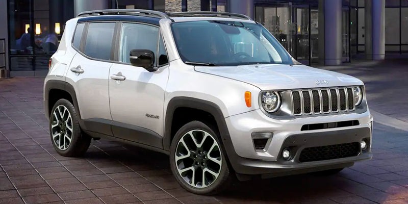 Silver 2022 Jeep Renegade Latitude SUV parked on a paved surface in front of a building at night.