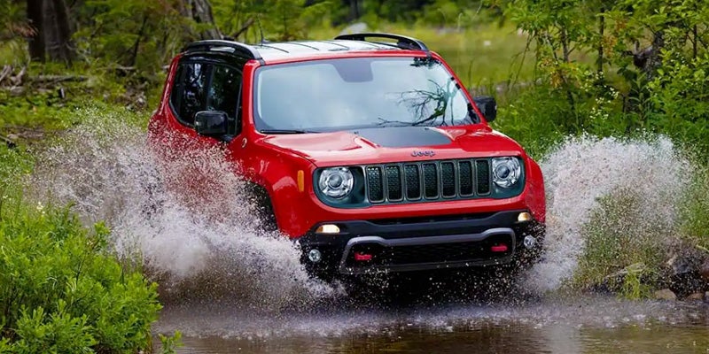 Red Jeep Renegade driving through a shallow body of water, splattering water high into the air.