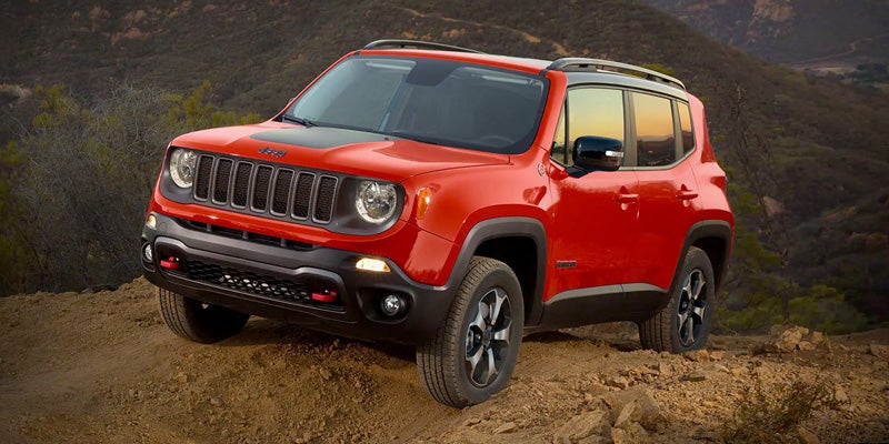 A fiery red Jeep Renegade SUV with a black roof and black accents, parked on a rocky desert trail.