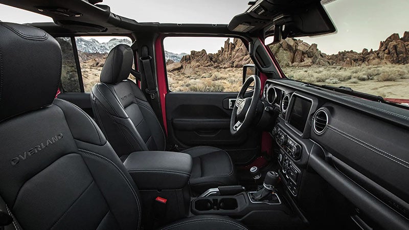 Interior view of a Jeep Wrangler, showing black leather seats and rocky desert landscape through open windows.