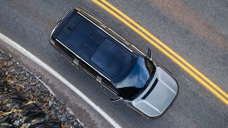 Overhead view of a gray car with a black roof driving on a winding cliffside road with double yellow lines.
