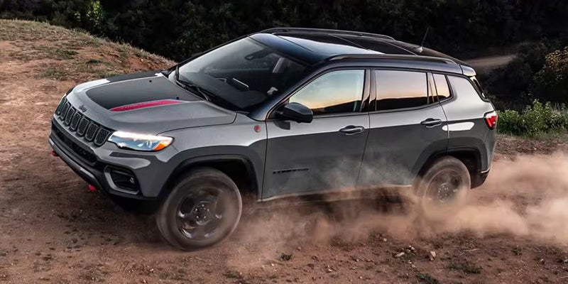 Gray Jeep Compass Trailhawk driving on a dirt road, kicking up dust plumes.
