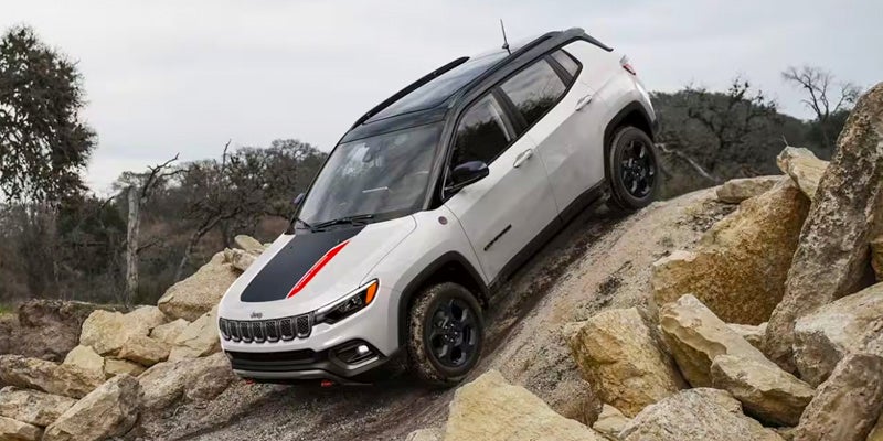 White Jeep Compass Trailhawk with black roof and hood stripe, climbing an incline over rocks.