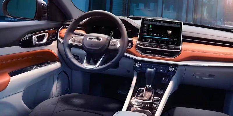 Interior front view of a Jeep vehicle with a modern dashboard featuring brown leather accents and a large touchscreen.