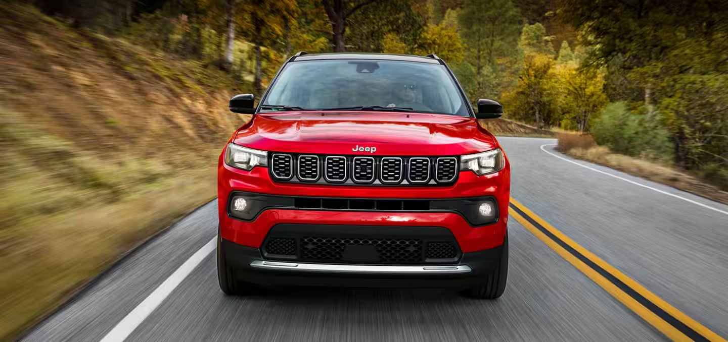 Front view of a red Jeep Compass driving on a winding, tree-lined road.