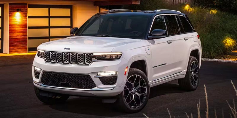 White 2022 Jeep Grand Cherokee 4xe parked in front of a modern house with illuminated garage doors.
