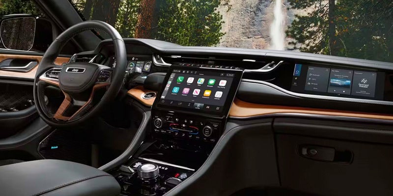 The dashboard of a Jeep Grand Cherokee with a large touchscreen display and another screen to the right, showing a waterfall.