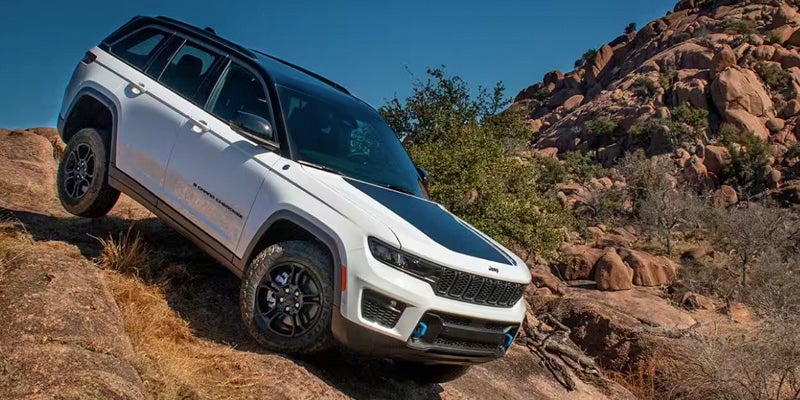 A white Jeep Grand Cherokee, with a black roof and hood accent, ascends a rocky incline.
