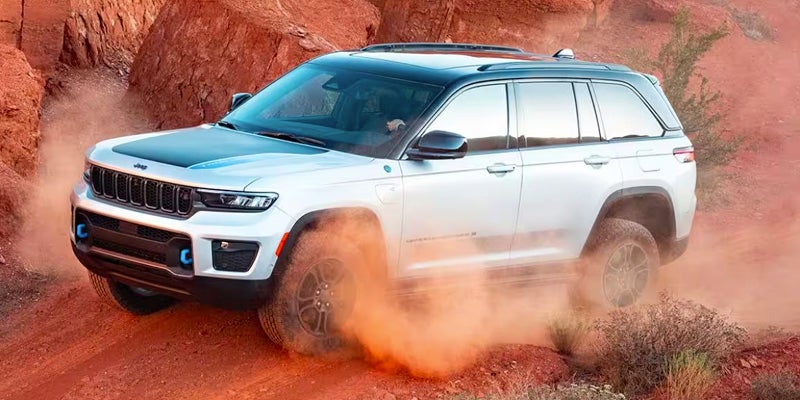 White Jeep Grand Cherokee 4xe kicking up red dust while off-roading in a desert landscape.