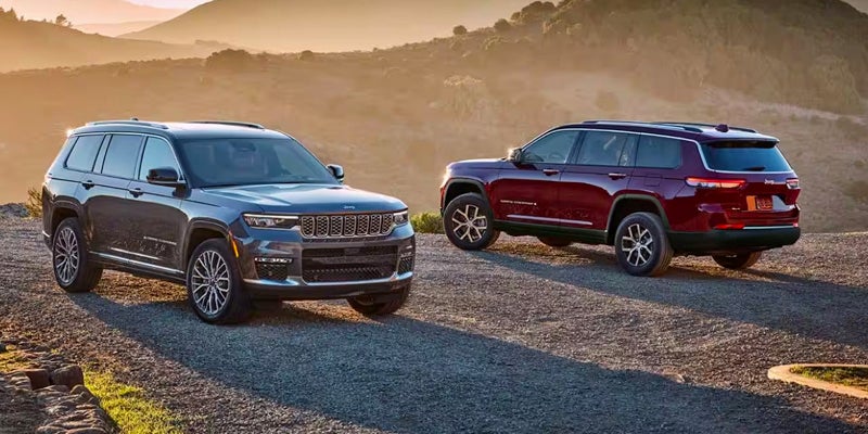 Two Jeep Grand Cherokee SUVs park on a gravel road at sunset. One gray, one maroon.