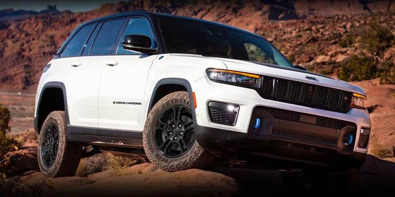 White Jeep Grand Cherokee 4xe Rubicon with black roof and wheels climbs a rocky, dirt trail.