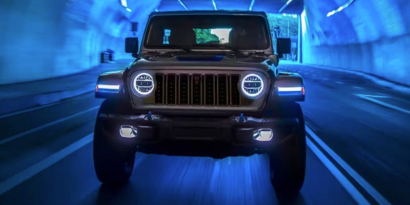 Front view of a Jeep Wrangler 4xe driving through a dark tunnel illuminated with blue light.