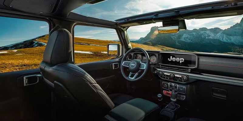 Driver's perspective inside a Jeep, showing the steering wheel, console, and a picturesque mountain landscape outside.