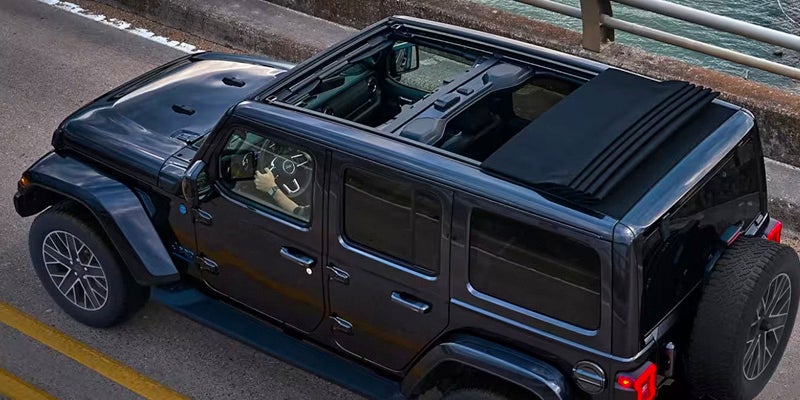 A black Jeep Wrangler from above, featuring an open powered soft top that's retracted over the rear passenger area.