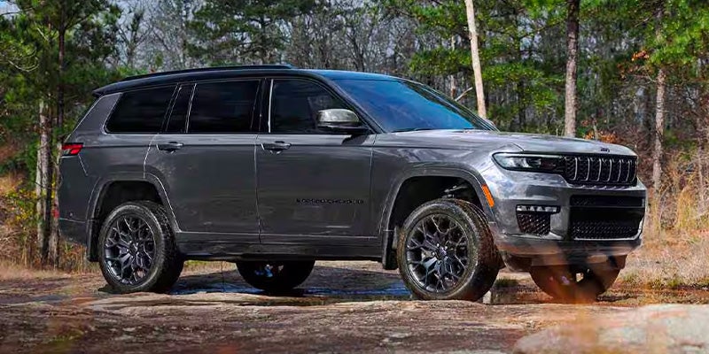 Gray Jeep Grand Cherokee L Limited parked on a dirt path in a wooded area.
